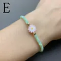 Detail shot of green shell beaded bracelet with pink daisy flower charm and gold beads. - Letter E