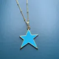 Detail view of gold star pendant necklace featuring vibrant blue enamel and sparkling zircon. - Style D