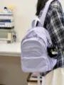 Detail view of a minimalist light purple casual backpack featuring a front pocket and plush charm. - With Charm / Purple