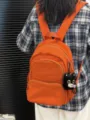 Close-up detail of casual orange backpack with cute cat pendant and front pocket design. - With Charm / Orange