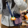 Detail shot of the grid fabric bucket bag worn crossbody, featuring a cute plush pumpkin charm. - Persimmon Kitten Pendant / Navy Blue