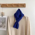 Blue cable knit scarf detail hanging on wooden rack with beige cardigan, cozy winter accessory. - Twist Cross Style / Klein Blue
