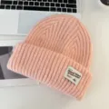 Close-up view of a cozy pink knit beanie featuring thick ribbed texture and a branded fabric patch. - Pink
