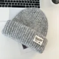 Close-up detail of gray wool knit beanie hat with brand label on white desktop scene. - Gray