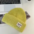 Close-up detail of the cozy green knit beanie showing soft textured yarn and brand label patch. - Yellow-Green