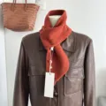 Knitted wool scarf detail showing soft texture, solid color cross wrap style, warm autumn wear. - Orange