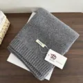 Detailed close-up shot of a soft grey knitted wool scarf folded neatly on a wooden table. - Gray