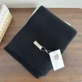 Black knit wool scarf detail showing soft texture and hanging tag. Perfect for winter warmth. - Black