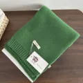 Green wool knit scarf texture detail, folded neatly on wooden table with brand tag. - Christmas Green