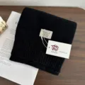 Close-up detail of a soft black wool knitted scarf folded neatly on a wooden surface. - Black