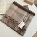 Detailed shot of a cozy plaid wool scarf with fringes, displayed on a wooden table setup. - Khaki Brown