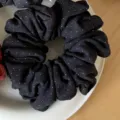 Close-up detail of dark brushed fabric scrunchie with tiny white dots resting on white plate. - 1# Black