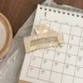 Detail shot of pearlescent acetate hair claw clip with metallic rim, displayed on calendar. - Mermaid Color