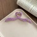 Detailed close-up of a purple acetate hair claw clip with unique heart shape and irregular wings. - Deep purple
