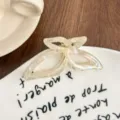 Close-up of translucent iridescent acetate butterfly hair claw clip on ceramic plate. - Mermaid White
