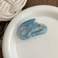 Close-up detail of blue iridescent irregular hair claw clip on white ceramic plate. - Metallic Blue