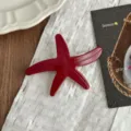 Detailed view of the red acetate starfish hair clip, showcasing glossy surface and spring clasp. - Red