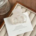 Close-up detail of the elegant white acetate hair claw clip on wooden display tray. - Pearl White