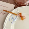 Close-up of elegant amber acetate bow hair clip resting on vintage ceramic plate. - Light Coffee