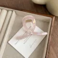 Close-up detail of a pink iridescent mermaid hair claw clip on white card and wooden tray. - Metallic Pink