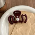 Detail view of dark red resin hair claw clip featuring a central pearl and metallic logo. - Angola Red