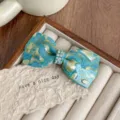 Detail view of acetate bow hair clip with sparkling rhinestones and blue marbled pattern. - Monet Blue