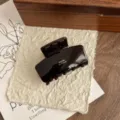 Detailed close-up of dark brown acetate hair claw clip, glossy shark clip with golden lettering. - Solid Square
