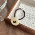 Detailed shot of retro acetate button hair tie on wooden tray with textured paper background. - Off White