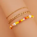 Primo piano di un set di 3 bracciali con catena d'oro e perline colorate per donna. - Giallo