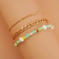 Vista dettagliata di un set di 3 bracciali stratificati con catene dorate e perle colorate. - Verde