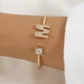 Primo piano dettagliato del bracciale aperto dorato con lettera M in strass al polso. - Lettera M Oro