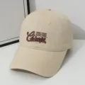 Close-up detail of beige cotton baseball cap with stylish brown embroidered lettering. - One Size / Khaki