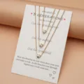 Collana a catena multistrato con tre ciondoli a cuore scintillanti su un biglietto augurale. - Collana Modello 0448 / Oro