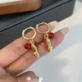 Close-up of gold-plated huggie hoop earrings with cute peanut pendant and red beads. - Red Bead Gold Peanut