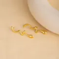 Detail shot of irregular wavy gold-colored stainless steel earrings on a textured beige surface. - E4911-2