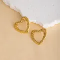 Close-up of textured gold heart earrings on a beige surface with white rock prop, detailed view. - E4698-1