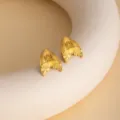 Close-up detail of unique gold mermaid tail earrings resting on modern sculpture prop. - E4762-1