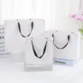 White paper gift bags set with black ribbon handles and elegant gold corner designs for festive gifting. - Medium Size 21x9x21cm / White Envelope Style