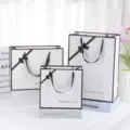 Elegant white gift bags with black borders and bows for cosmetics, holidays, and parties. - White