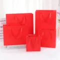 Red paper gift bags set with ribbon handles for festive packaging, cosmetics and retail use. - Festive Red