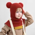 Detailed shot of a cute toddler wearing a red knitted balaclava hat with double pom poms. - 2-6 Years Old / Burgundy