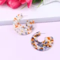 Close-up detail of stylish C-shaped acrylic geometric terrazzo earrings with colorful glitter flakes. - Color 2