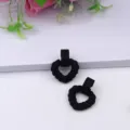 Detailed close-up view of black twisted heart stud earrings, matte acrylic geometric fashion jewelry. - Black
