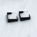Close-up detail of modern black geometric open hoop earrings on white fluffy fur background. - Simple Square