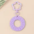 Vue détaillée du porte-clés en acrylique rond violet avec fermoir fleur et texture tissée. - Violet