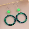 Detail view of green marbled acrylic hoop earrings featuring vibrant beads and metal hooks. - Green