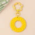 Gros plan détaillé du charmant pendentif de porte-clés rond tissé jaune vif avec fermoir fleur. - Jaune