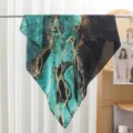 Detail view of green abstract printed square scarf hanging on rod, stylish textile. - Emerald Green