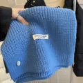 Knit scarf detail shot showing soft blue wool texture and handmade label decoration. - Blue