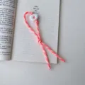 Nahaufnahme Detailansicht des rosa gewebten Handy-Schlüsselband-Anhängers auf Buch. - Orange
